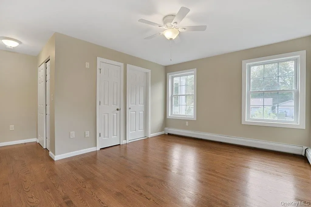 Unfurnished bedroom featuring wood finished floors, two closets, a baseboard heating unit, and a ceiling fan Unfurnished bedroom featuring wood finished floors, two closets, a baseboard heating unit, and a ceiling fan