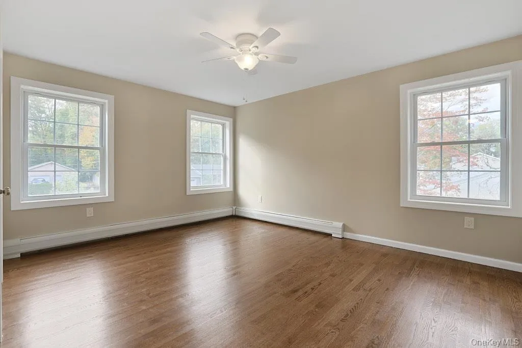 Unfurnished room featuring wood finished floors, baseboard heating, a baseboard radiator, and a ceiling fan Unfurnished room featuring wood finished floors, baseboard heating, a baseboard radiator, and a ceiling fan