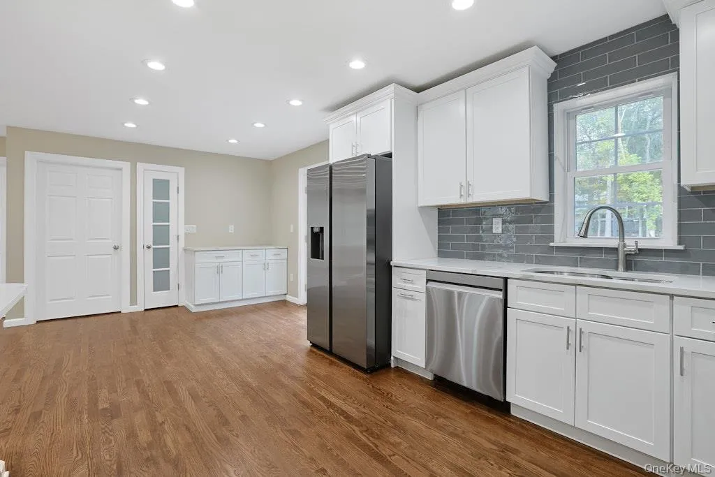 Kitchen with white cabinetry, stainless steel appliances, backsplash, recessed lighting, and dark wood-style floors Kitchen with white cabinetry, stainless steel appliances, backsplash, recessed lighting, and dark wood-style floors