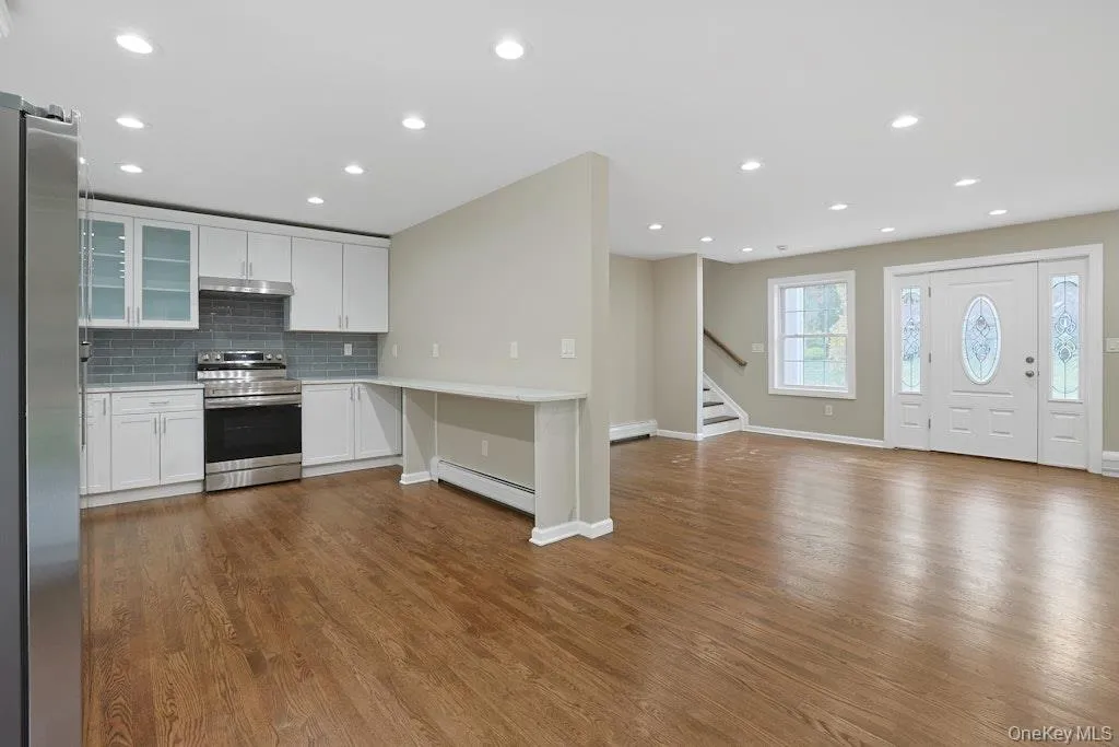 Kitchen featuring glass insert cabinets, open floor plan, white cabinetry, stainless steel appliances, and tasteful backsplash Kitchen featuring glass insert cabinets, open floor plan, white cabinetry, stainless steel appliances, and tasteful backsplash