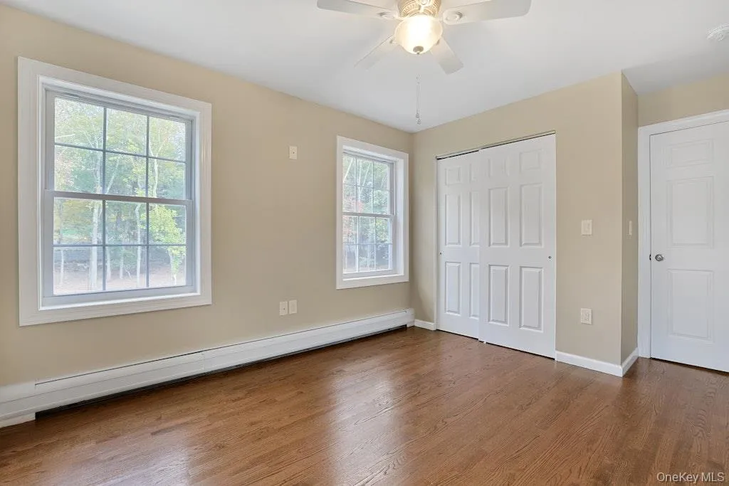 Unfurnished bedroom with a baseboard radiator, wood finished floors, ceiling fan, and a closet Unfurnished bedroom with a baseboard radiator, wood finished floors, ceiling fan, and a closet