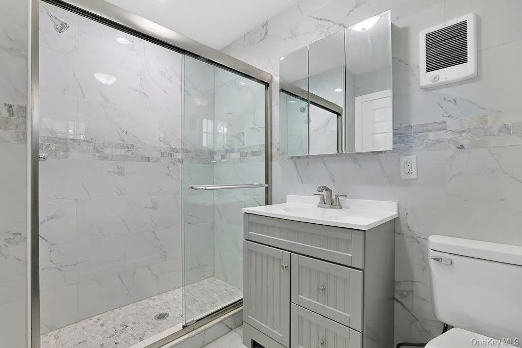 Bathroom with a marble finish shower, tile walls, vanity, and heating unit Bathroom with a marble finish shower, tile walls, vanity, and heating unit