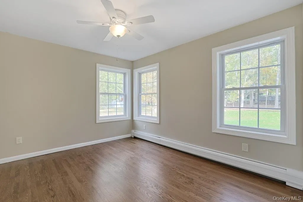 Unfurnished room with a baseboard radiator, wood finished floors, and a ceiling fan Unfurnished room with a baseboard radiator, wood finished floors, and a ceiling fan