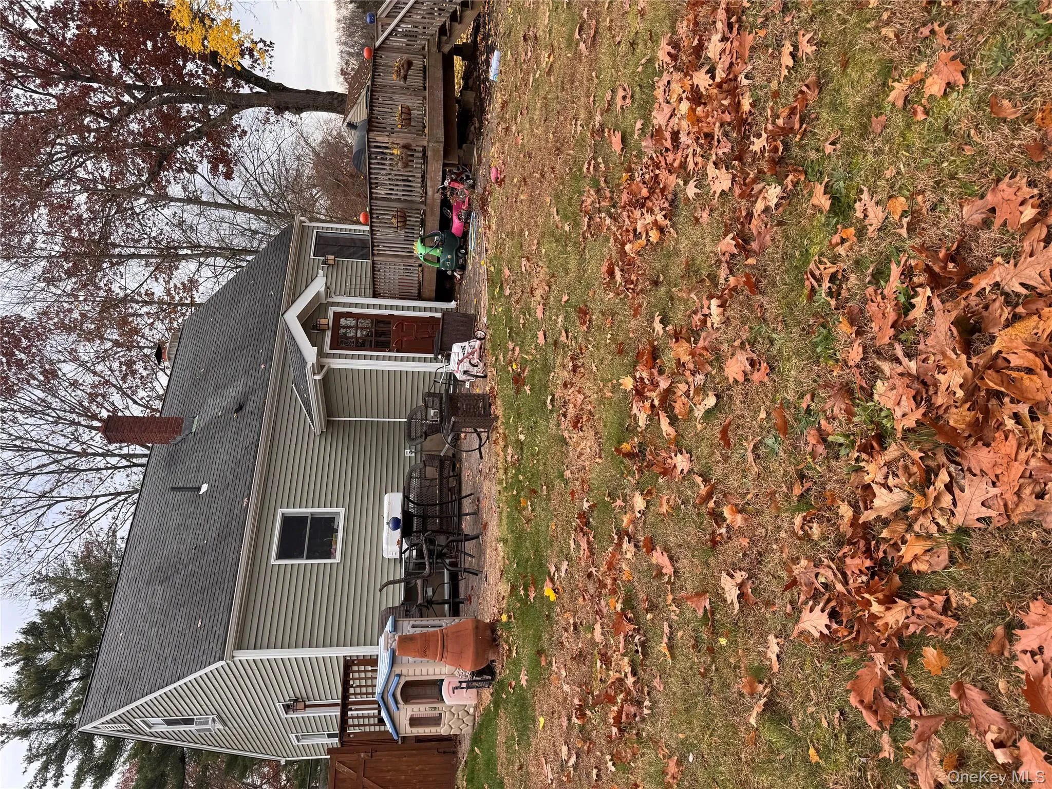 Rear view of house with a chimney, a patio area, a shingled roof, a wooden deck, and a yard Rear view of house with a chimney, a patio area, a shingled roof, a wooden deck, and a yard