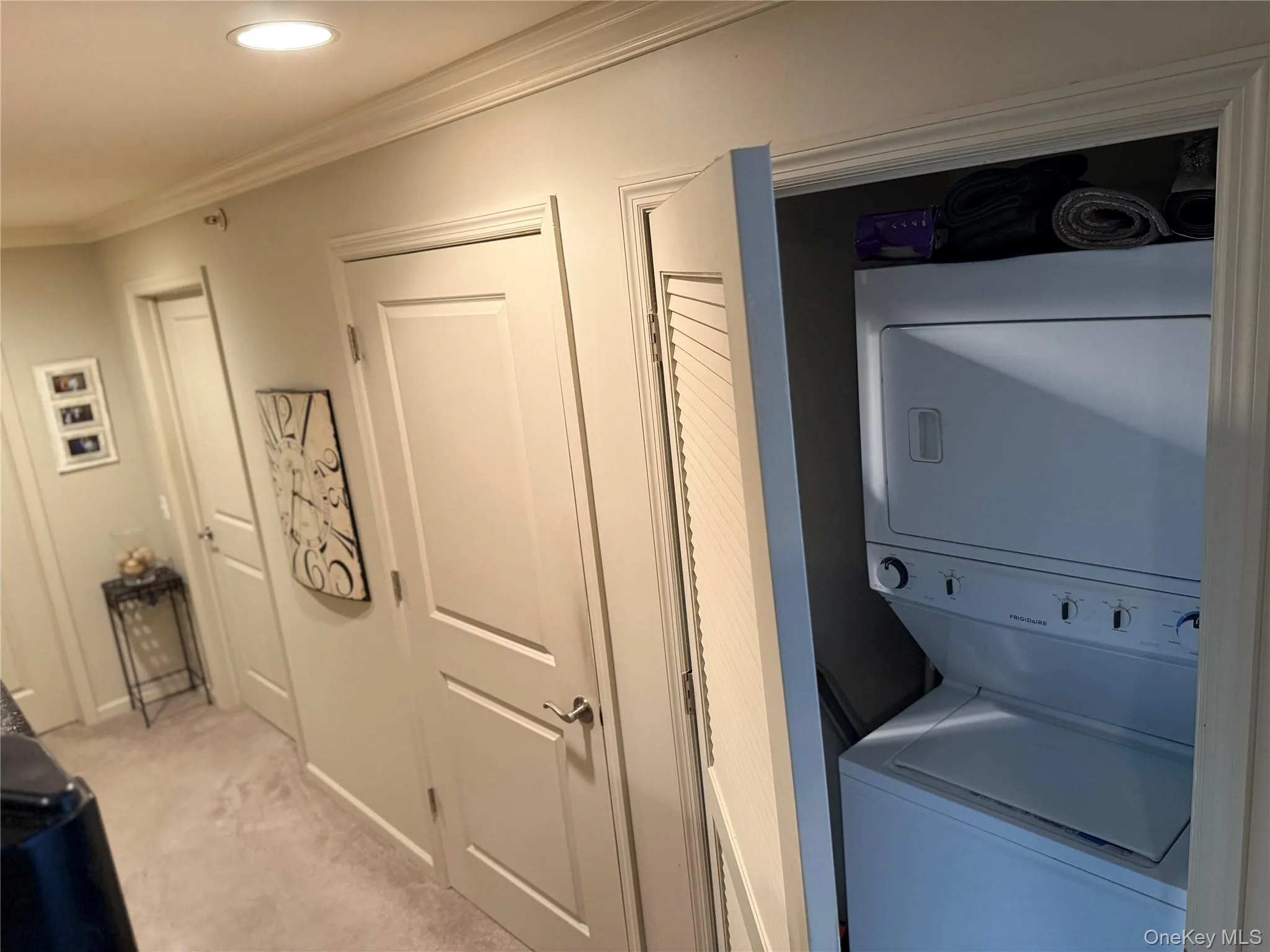 Washroom with carpet flooring, stacked washer and clothes dryer, ornamental molding, and recessed lighting. Washroom with carpet flooring, stacked washer and clothes dryer, ornamental molding, and recessed lighting.