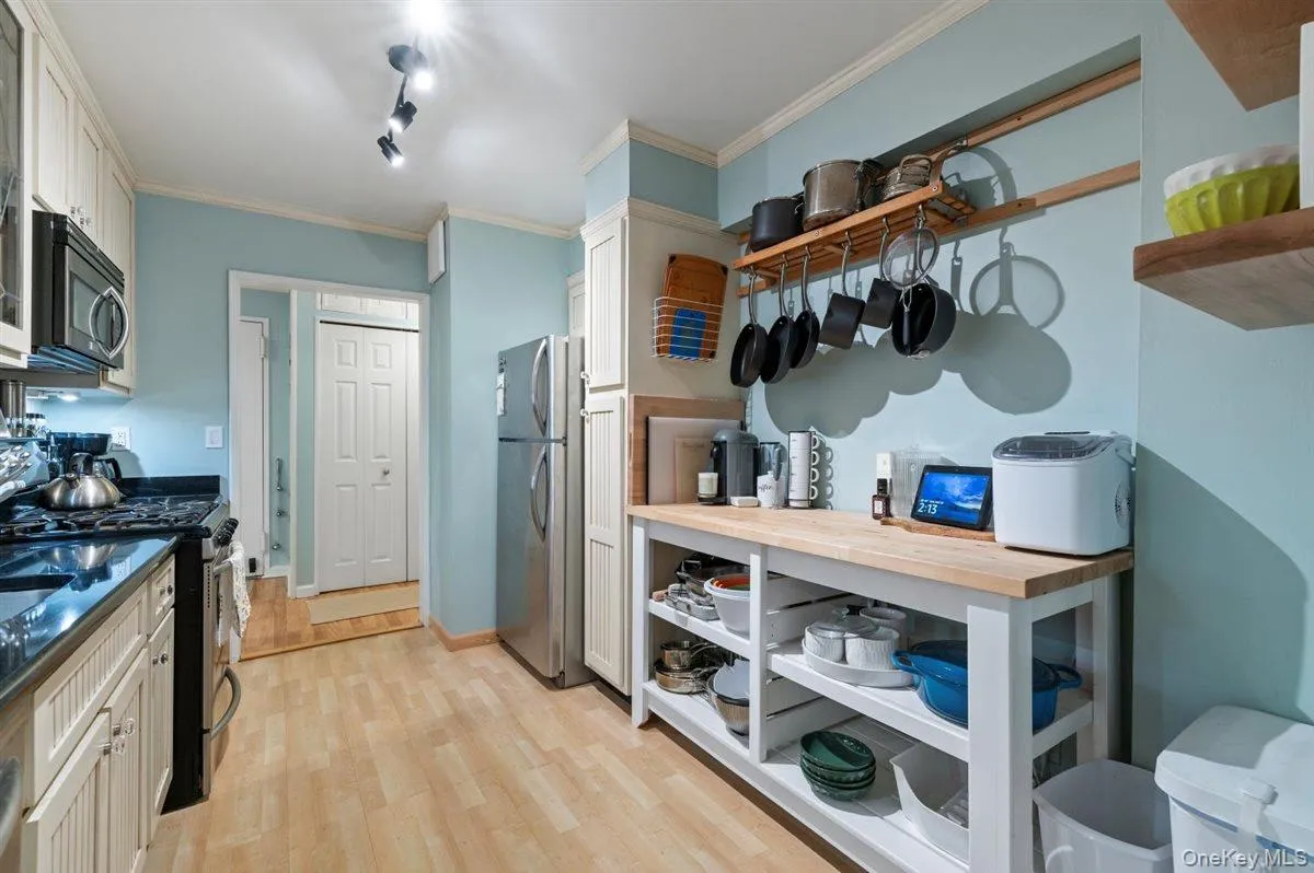 Kitchen featuring appliances with stainless steel finishes, track lighting, ornamental molding, light wood-style flooring, and open shelves Kitchen featuring appliances with stainless steel finishes, track lighting, ornamental molding, light wood-style flooring, and open shelves