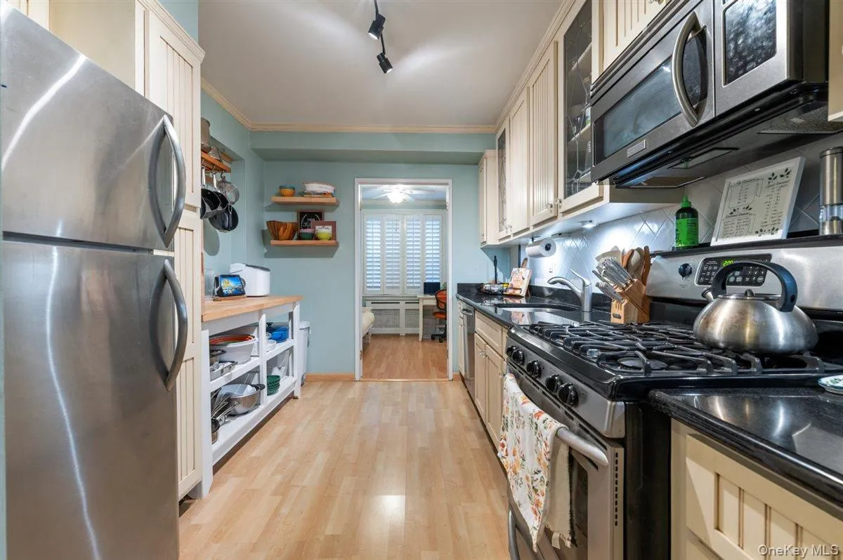 Kitchen with appliances with stainless steel finishes, light wood finished floors, open shelves, ornamental molding, and rail lighting Kitchen with appliances with stainless steel finishes, light wood finished floors, open shelves, ornamental molding, and rail lighting