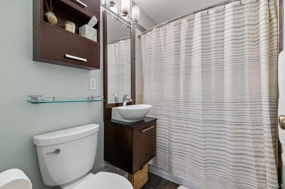Full bath featuring curtained shower, vanity, and dark tile patterned floors Full bath featuring curtained shower, vanity, and dark tile patterned floors