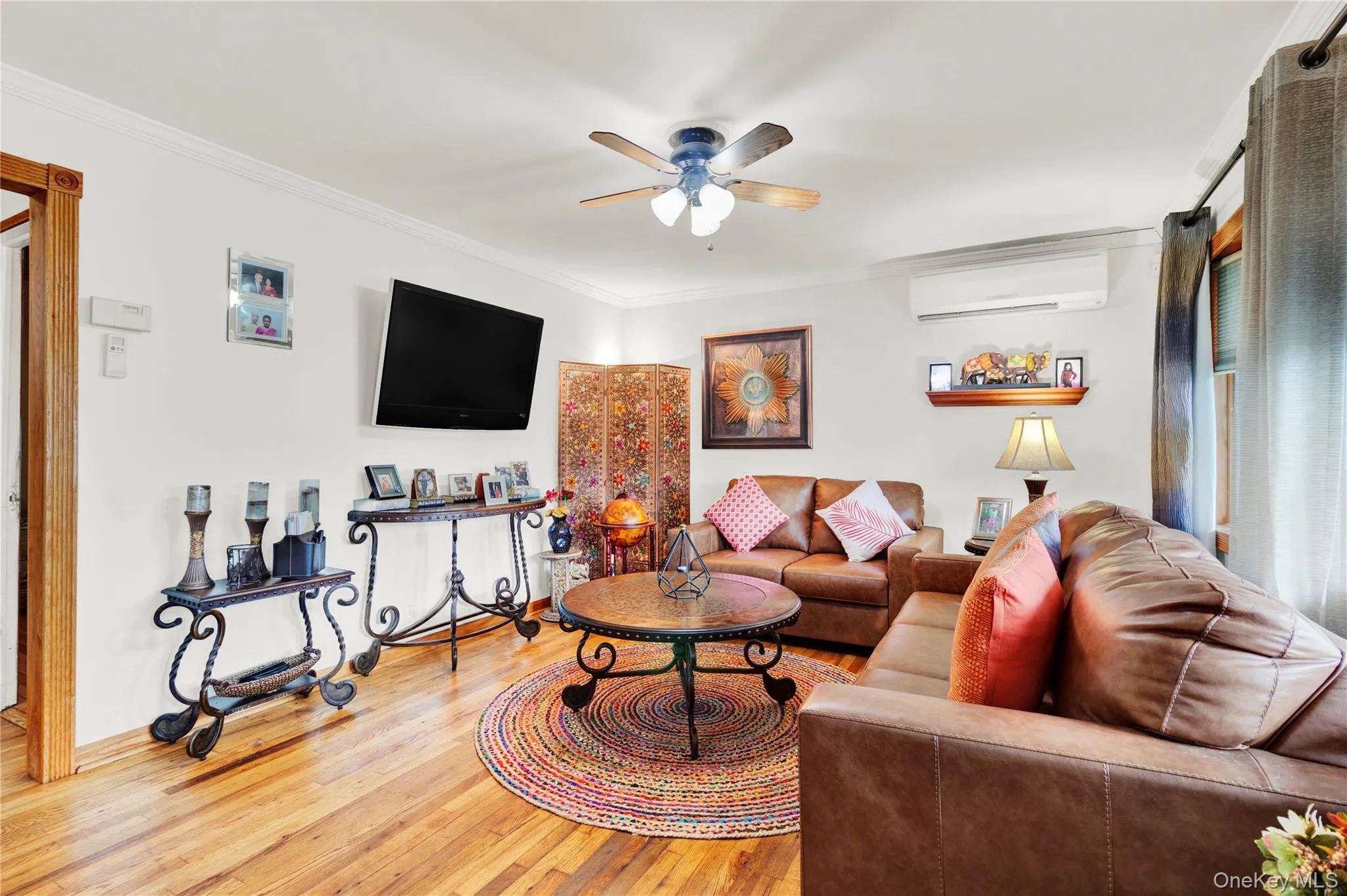 Living room featuring hardwood / wood-style flooring, ornamental molding, an AC wall unit, and ceiling fan Living room featuring hardwood / wood-style flooring, ornamental molding, an AC wall unit, and ceiling fan