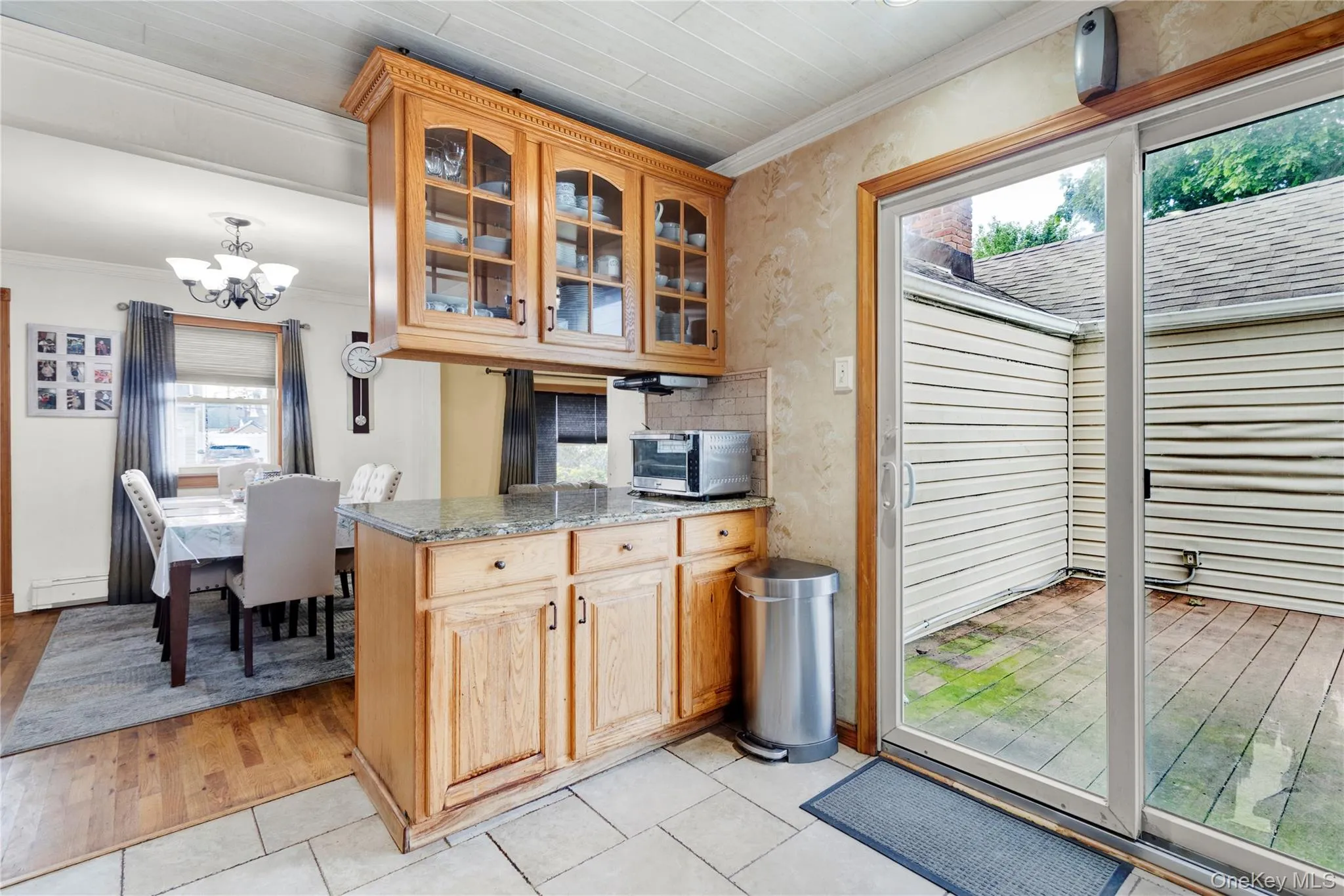 Kitchen featuring crown molding, light stone counters, a chandelier, light tile patterned flooring, and glass insert cabinets Kitchen featuring crown molding, light stone counters, a chandelier, light tile patterned flooring, and glass insert cabinets