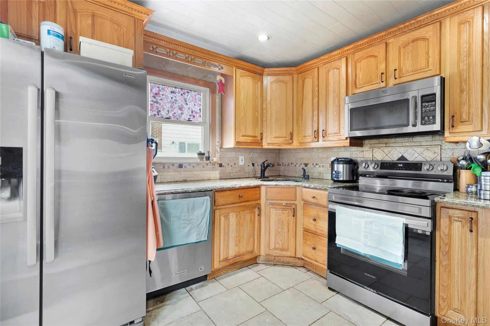 Kitchen with appliances with stainless steel finishes, light stone countertops, decorative backsplash, light tile patterned floors, and recessed lighting Kitchen with appliances with stainless steel finishes, light stone countertops, decorative backsplash, light tile patterned floors, and recessed lighting