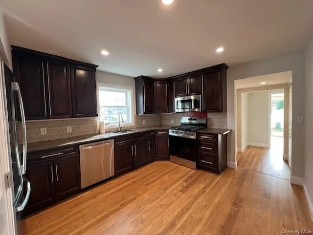 Kitchen with appliances with stainless steel finishes, dark brown cabinets, tasteful backsplash, light wood-style floors, and recessed lighting Kitchen with appliances with stainless steel finishes, dark brown cabinets, tasteful backsplash, light wood-style floors, and recessed lighting