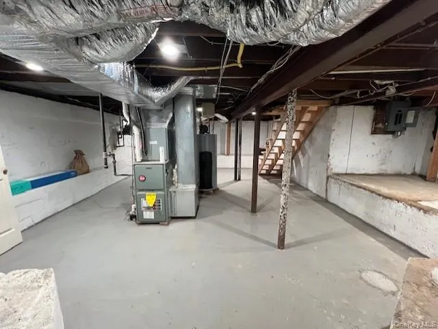 Unfinished below grade area with stairs, heating unit, water heater, and electric panel Unfinished below grade area with stairs, heating unit, water heater, and electric panel