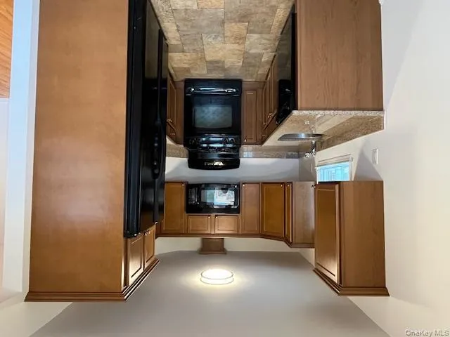 Kitchen with black appliances, light stone countertops, stone finish floors, and brown cabinets Kitchen with black appliances, light stone countertops, stone finish floors, and brown cabinets