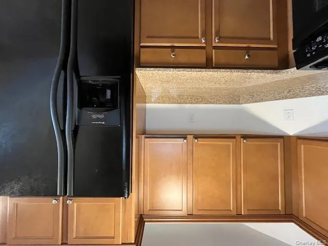 Kitchen featuring fridge, light stone counters, brown cabinetry, and black stove Kitchen featuring fridge, light stone counters, brown cabinetry, and black stove