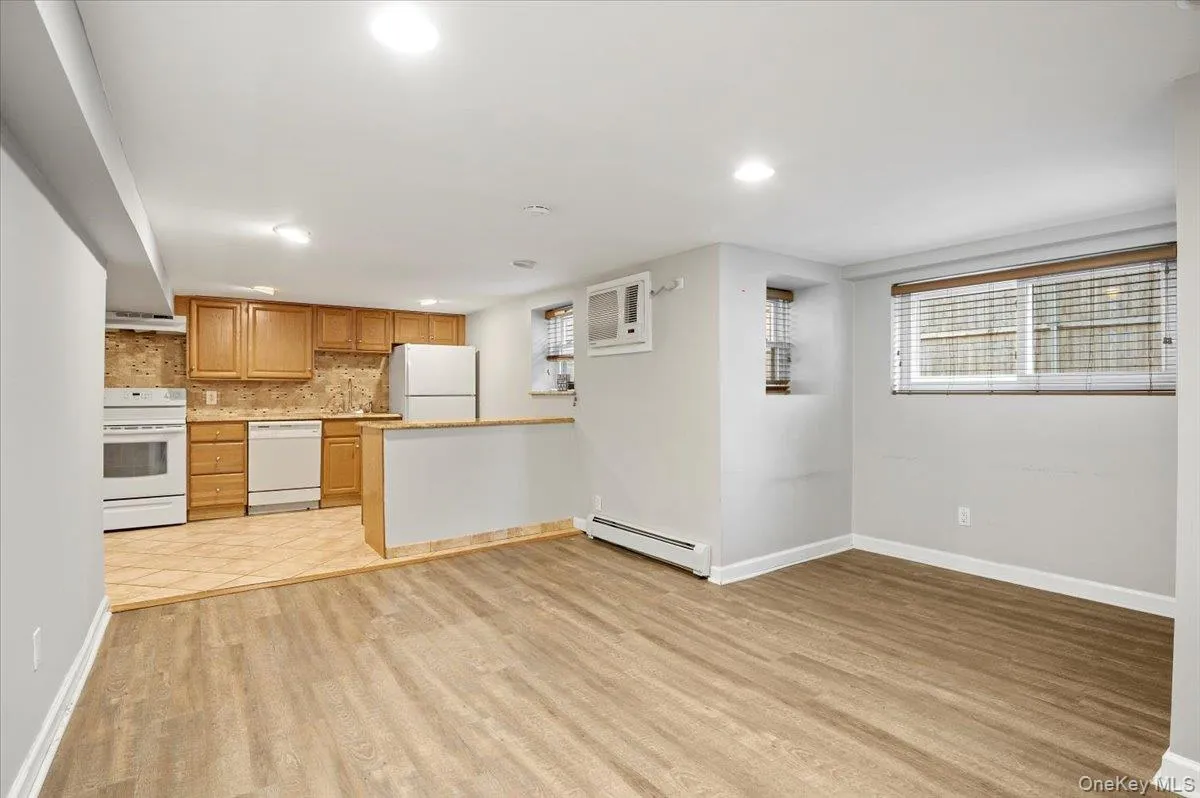 Kitchen with white appliances, light wood finished floors, light countertops, baseboard heating, and decorative backsplash Kitchen with white appliances, light wood finished floors, light countertops, baseboard heating, and decorative backsplash