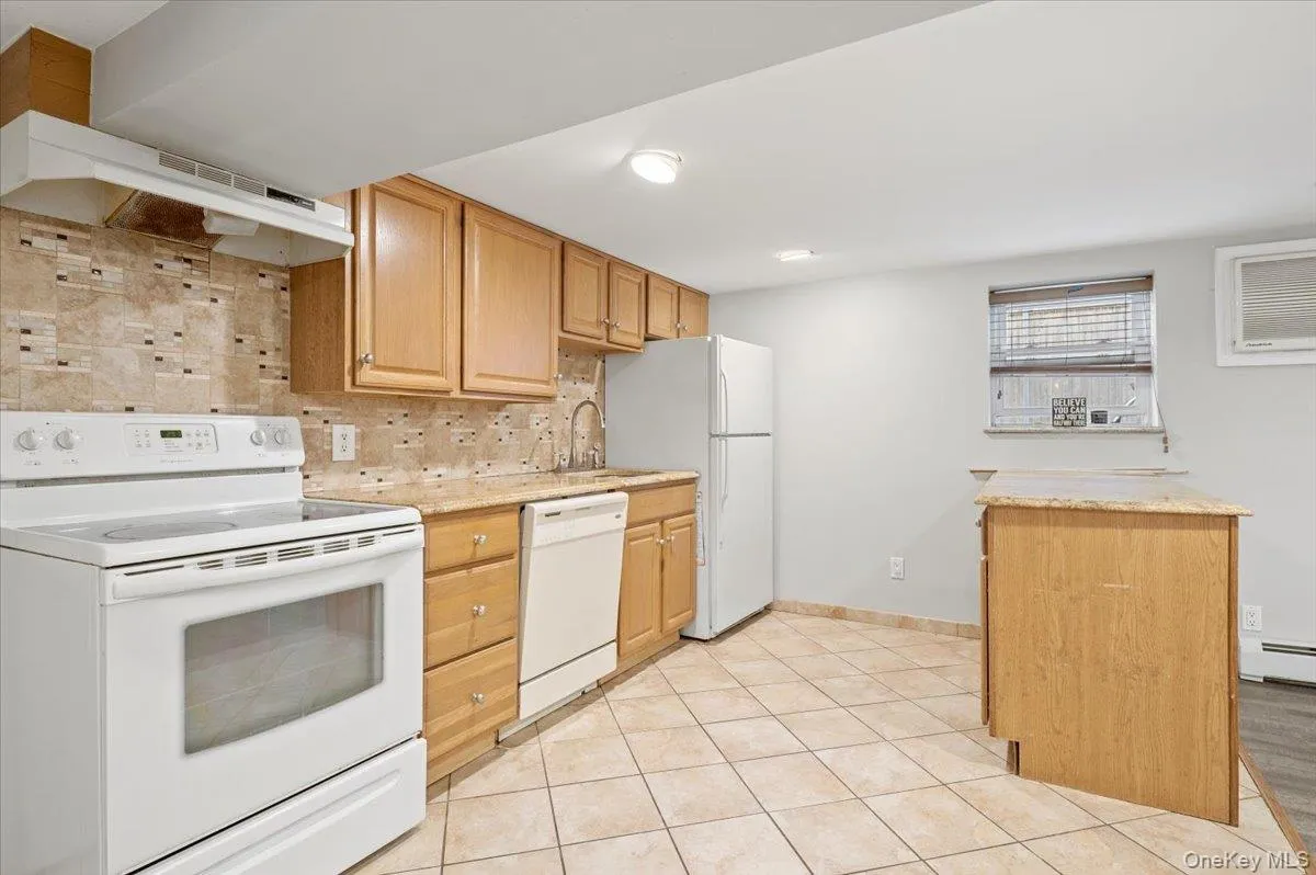 Kitchen with white appliances, decorative backsplash, light tile patterned floors, under cabinet range hood, and light stone counters Kitchen with white appliances, decorative backsplash, light tile patterned floors, under cabinet range hood, and light stone counters