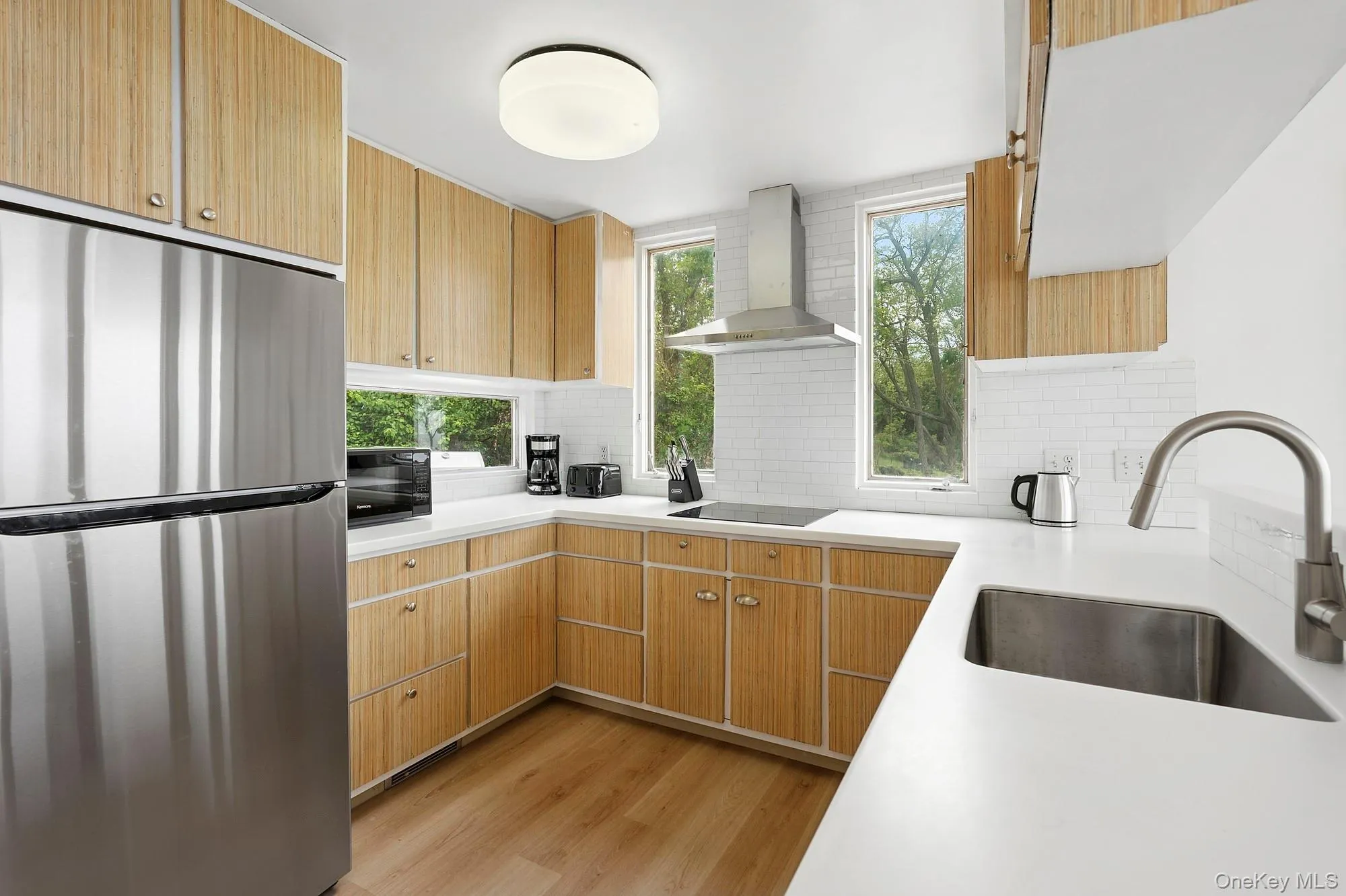 Kitchen featuring black appliances, wall chimney range hood, plenty of natural light, and light wood-style flooring Kitchen featuring black appliances, wall chimney range hood, plenty of natural light, and light wood-style flooring