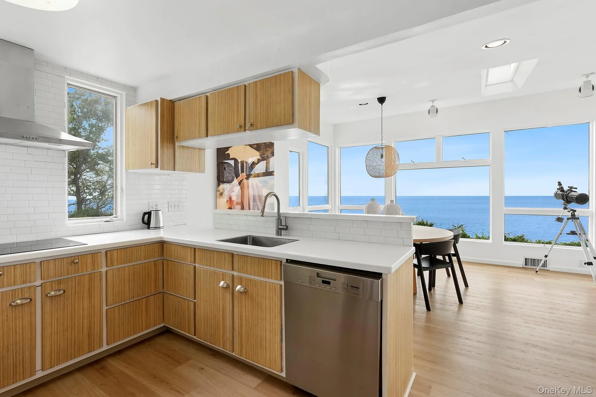 Kitchen with wall chimney exhaust hood, stainless steel dishwasher, pendant lighting, light wood-type flooring, and decorative backsplash Kitchen with wall chimney exhaust hood, stainless steel dishwasher, pendant lighting, light wood-type flooring, and decorative backsplash