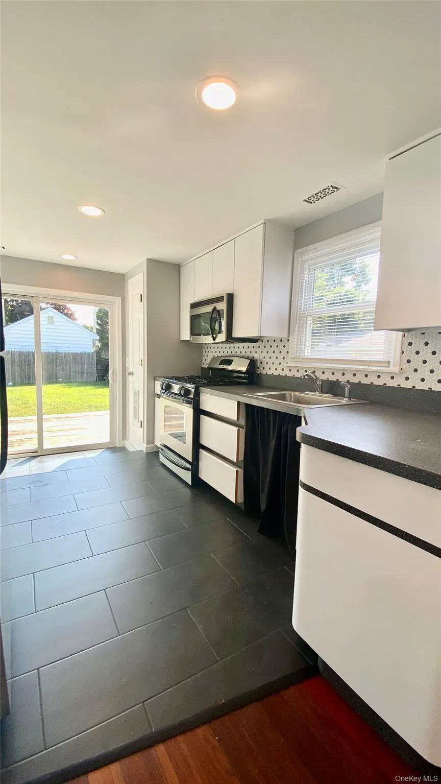 Kitchen featuring white cabinets, stainless steel appliances, plenty of natural light, and tasteful backsplash Kitchen featuring white cabinets, stainless steel appliances, plenty of natural light, and tasteful backsplash