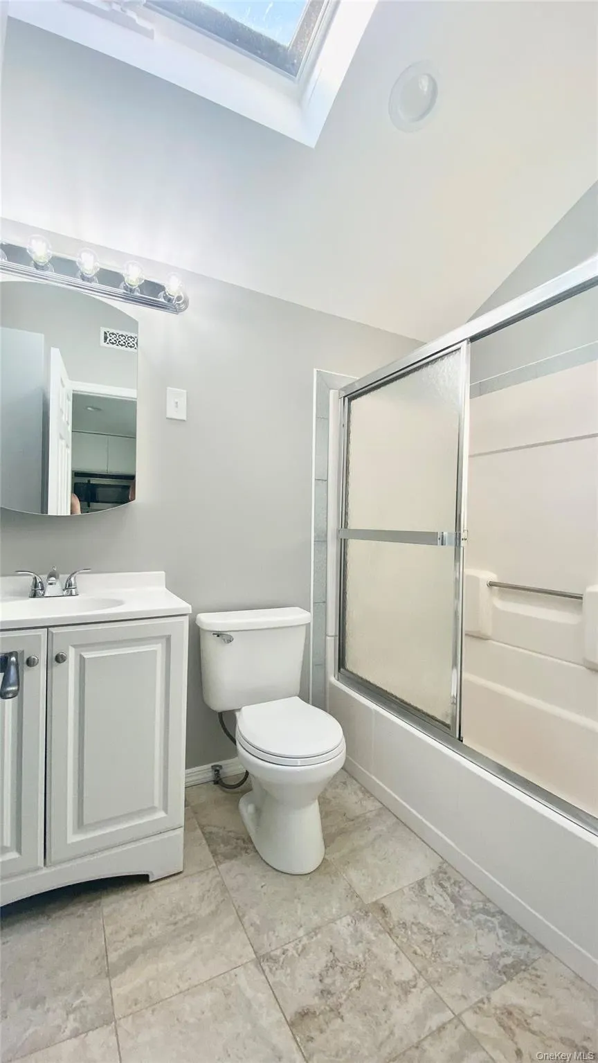 Full bathroom with vanity, combined bath / shower with glass door, a skylight, and lofted ceiling Full bathroom with vanity, combined bath / shower with glass door, a skylight, and lofted ceiling