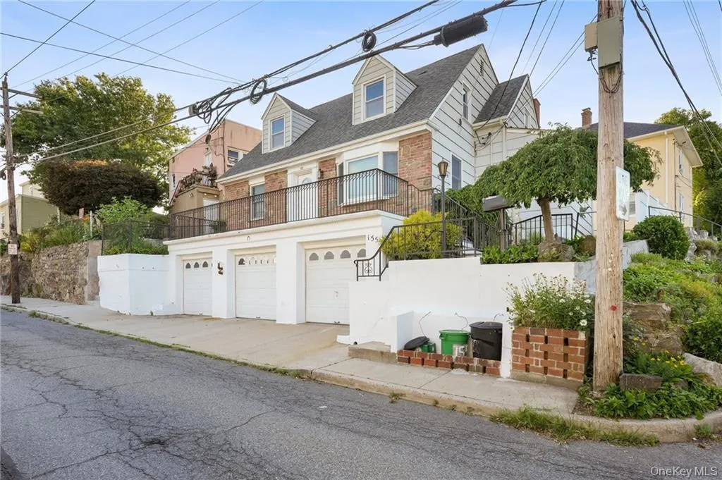 Cape cod home featuring a balcony, brick siding, a garage, and driveway Cape cod home featuring a balcony, brick siding, a garage, and driveway