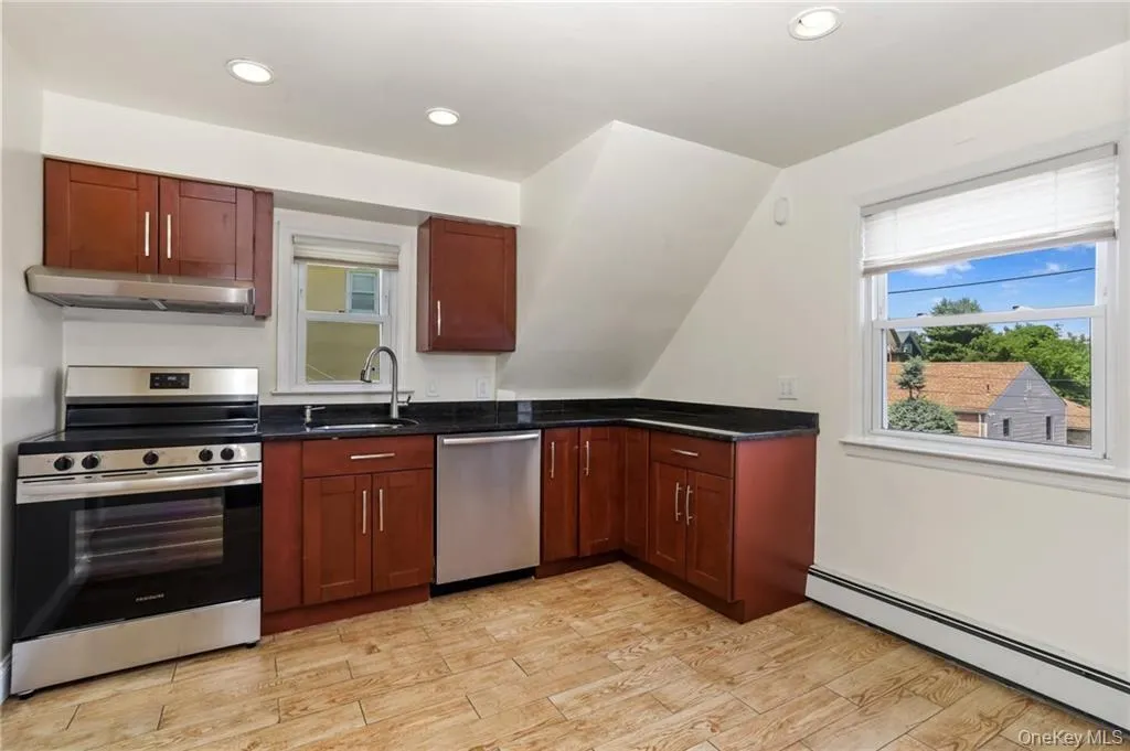 Kitchen featuring appliances with stainless steel finishes, baseboard heating, under cabinet range hood, dark stone counters, and light wood-type flooring Kitchen featuring appliances with stainless steel finishes, baseboard heating, under cabinet range hood, dark stone counters, and light wood-type flooring