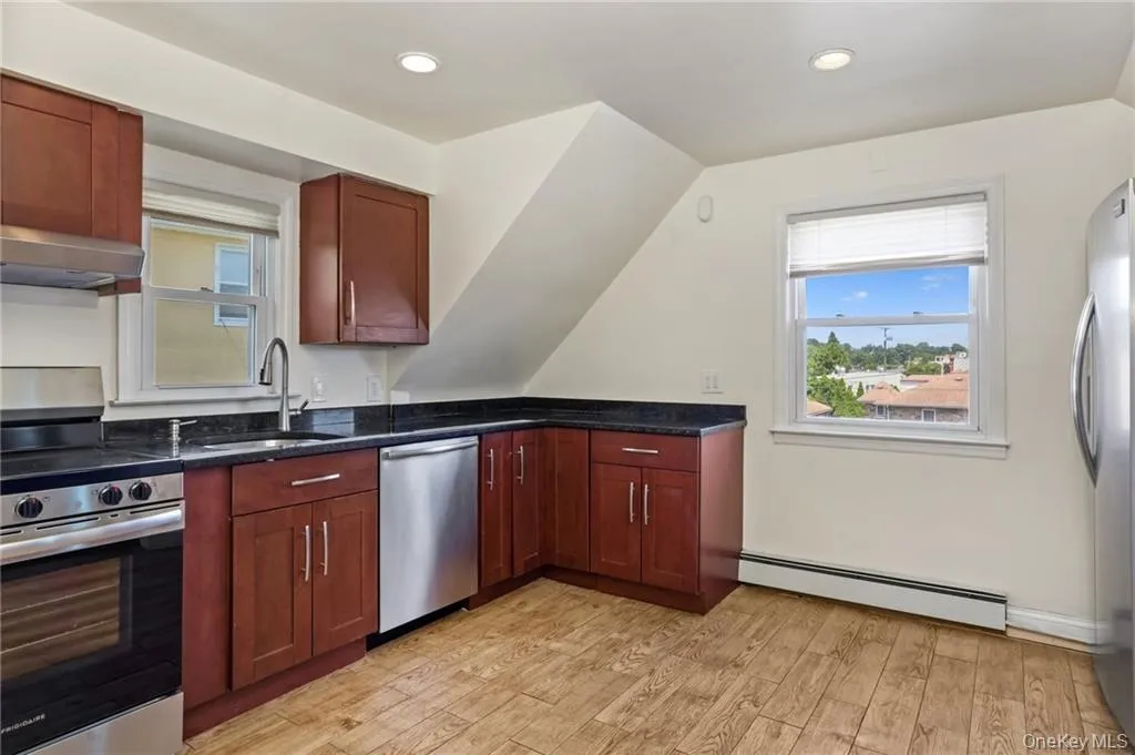 Kitchen featuring stainless steel appliances, baseboard heating, light wood-type flooring, exhaust hood, and plenty of natural light Kitchen featuring stainless steel appliances, baseboard heating, light wood-type flooring, exhaust hood, and plenty of natural light