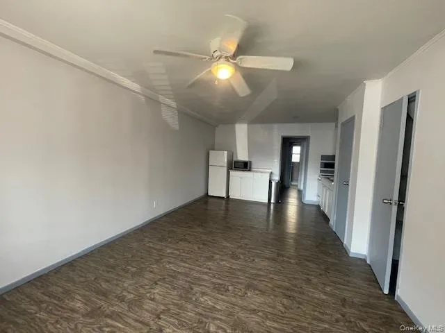 Unfurnished living room featuring dark wood-style flooring, ceiling fan, and crown molding Unfurnished living room featuring dark wood-style flooring, ceiling fan, and crown molding
