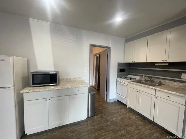 Kitchen with white appliances, white cabinets, dark wood-style floors, ornamental molding, and light stone countertops Kitchen with white appliances, white cabinets, dark wood-style floors, ornamental molding, and light stone countertops