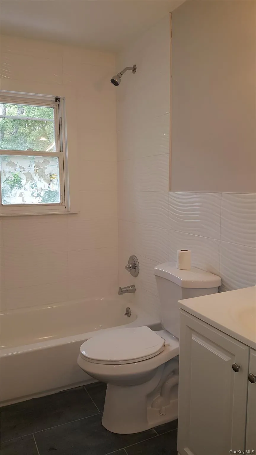 Bathroom featuring vanity, bathing tub / shower combination, tile walls, and dark tile patterned floors Bathroom featuring vanity, bathing tub / shower combination, tile walls, and dark tile patterned floors