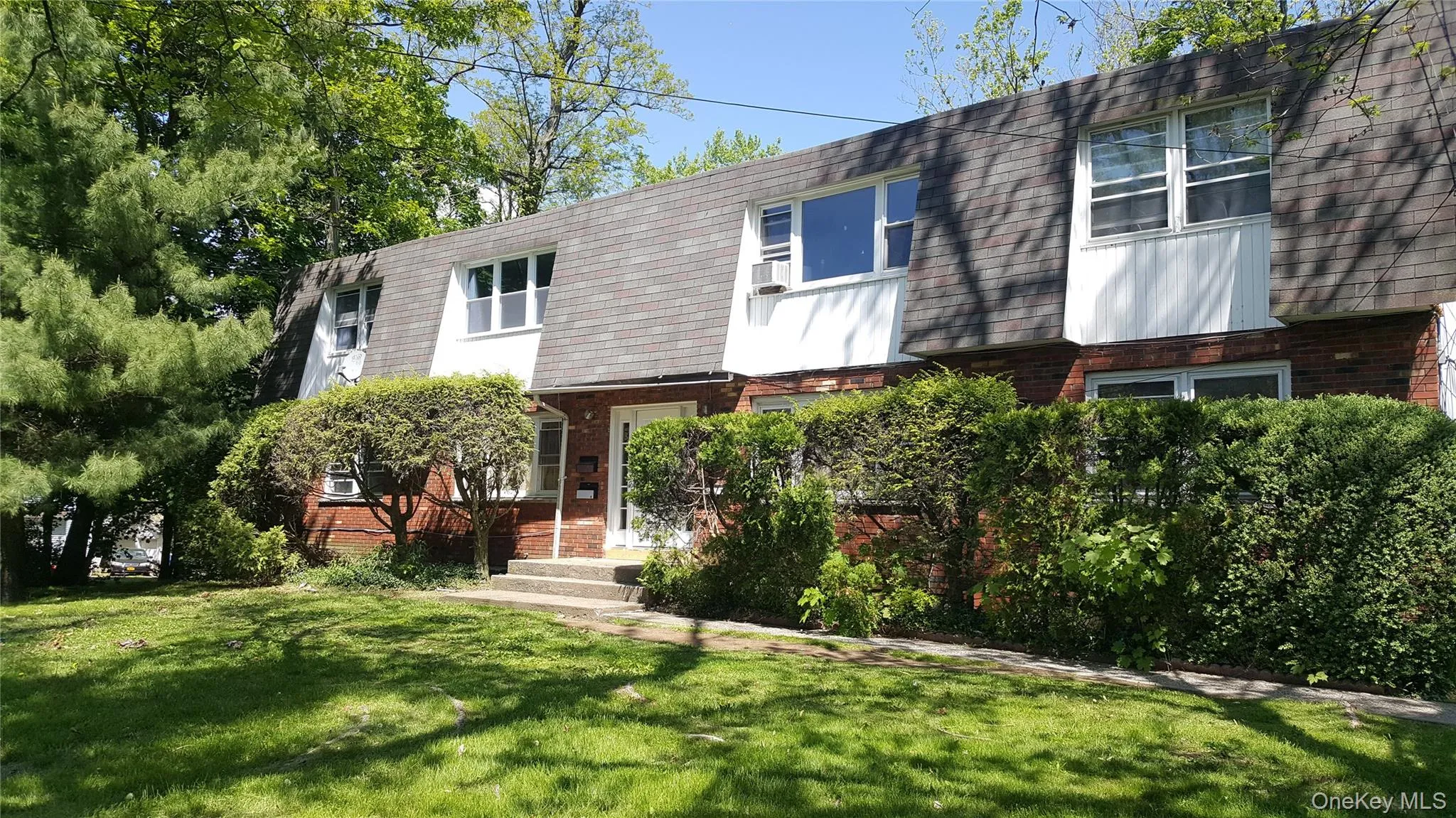 View of front of house with mansard roof, brick siding, a front yard, and a shingled roof View of front of house with mansard roof, brick siding, a front yard, and a shingled roof