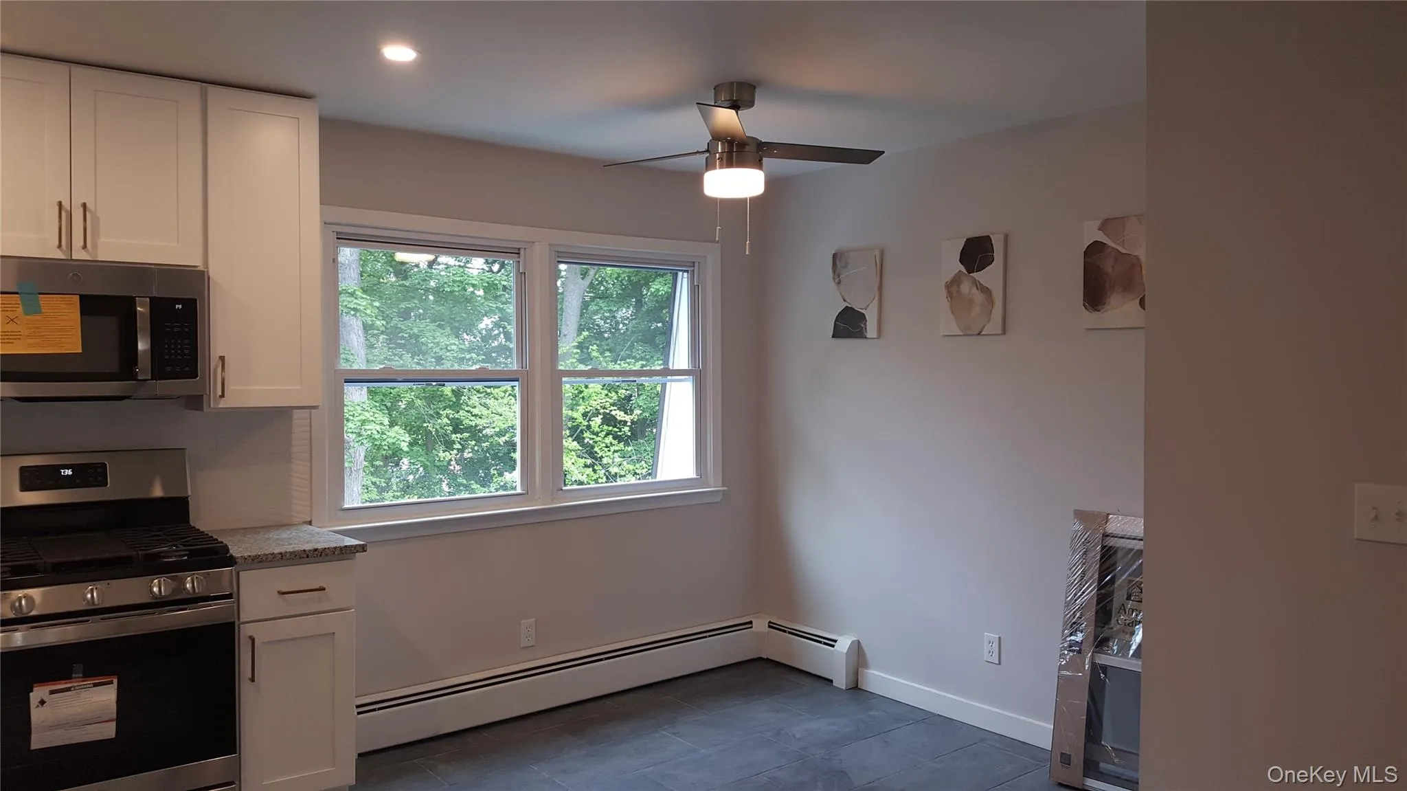 Kitchen featuring stainless steel appliances, white cabinetry, a baseboard heating unit, light stone counters, and a ceiling fan Kitchen featuring stainless steel appliances, white cabinetry, a baseboard heating unit, light stone counters, and a ceiling fan