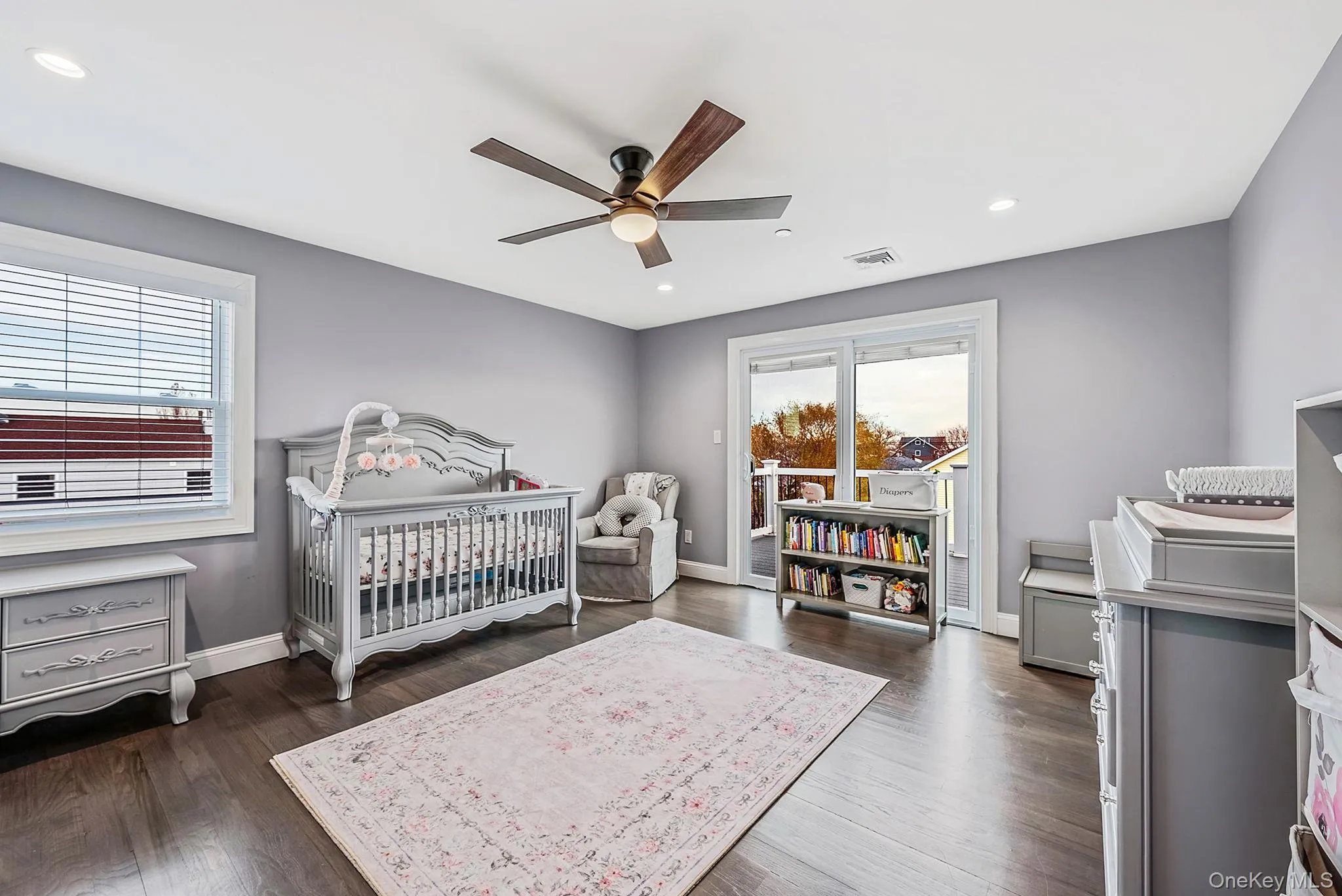 Bedroom with multiple windows, a ceiling fan, recessed lighting, a crib, and dark wood-style floors Bedroom with multiple windows, a ceiling fan, recessed lighting, a crib, and dark wood-style floors