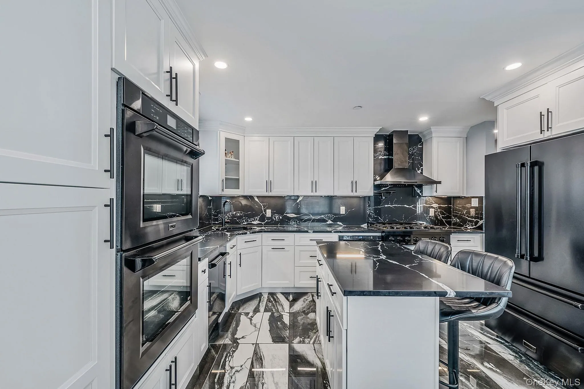Kitchen featuring a kitchen bar, double wall oven, dark marble finish floors, tasteful backsplash, and white cabinetry Kitchen featuring a kitchen bar, double wall oven, dark marble finish floors, tasteful backsplash, and white cabinetry