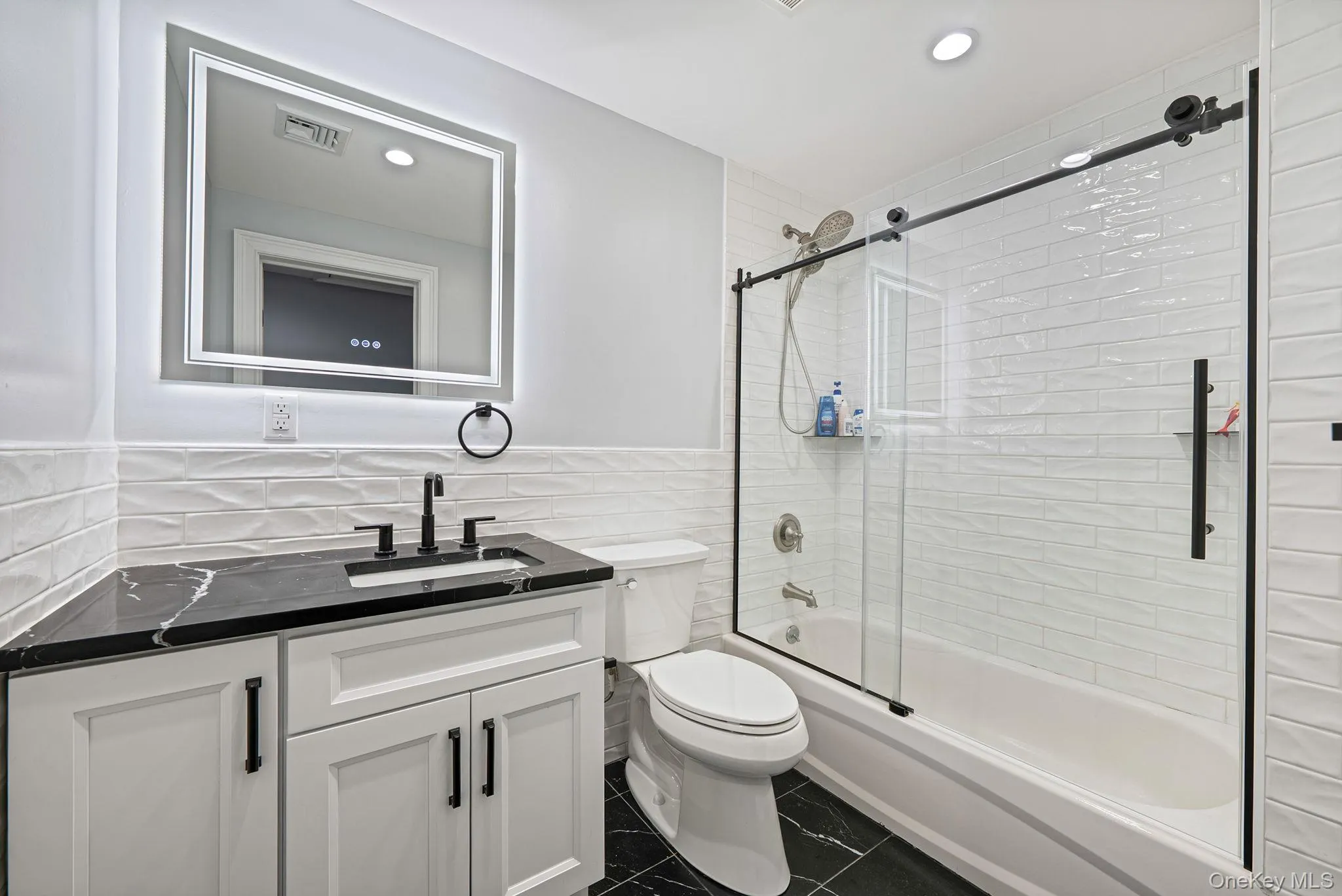 Bathroom with vanity, shower / bath combination with glass door, dark tile patterned floors, recessed lighting, and tile walls Bathroom with vanity, shower / bath combination with glass door, dark tile patterned floors, recessed lighting, and tile walls