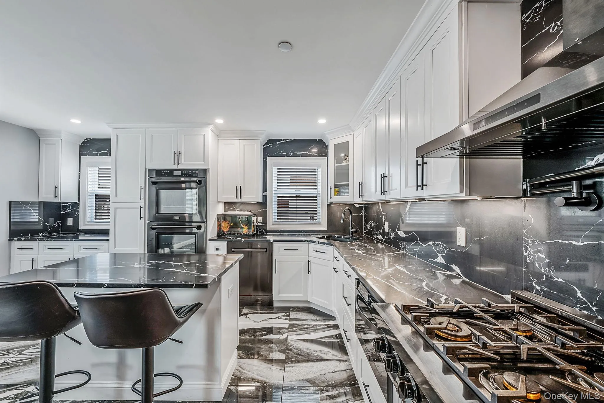 Kitchen featuring decorative backsplash, dark marble finish floors, ventilation hood, white cabinets, and a kitchen breakfast bar Kitchen featuring decorative backsplash, dark marble finish floors, ventilation hood, white cabinets, and a kitchen breakfast bar