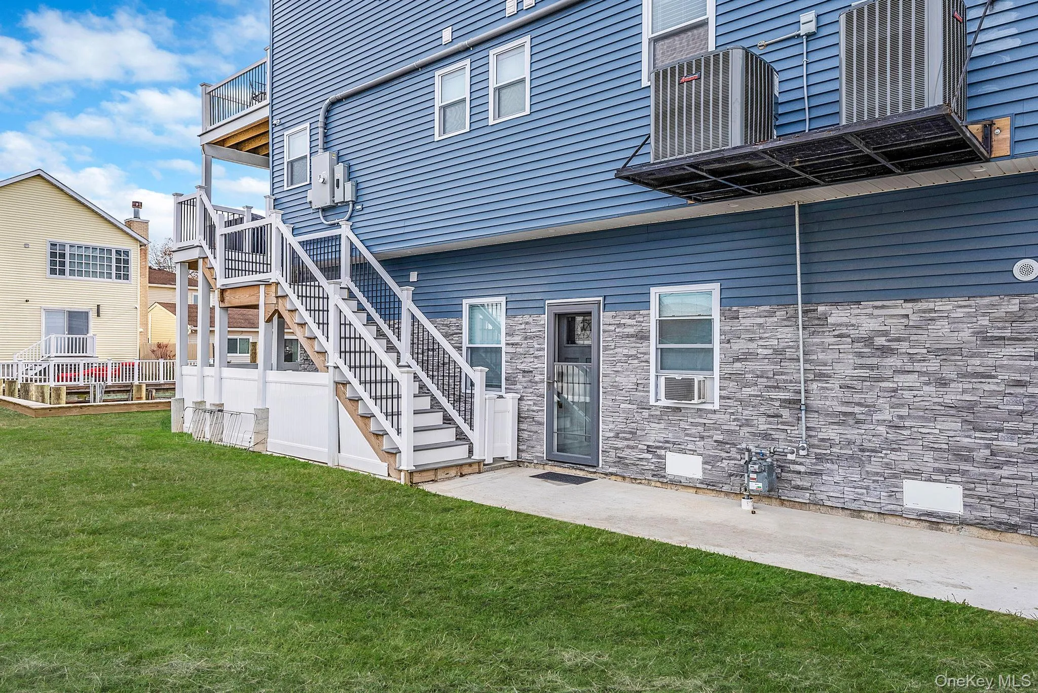 Rear view of property with a lawn, stone siding, a patio area, and stairs Rear view of property with a lawn, stone siding, a patio area, and stairs