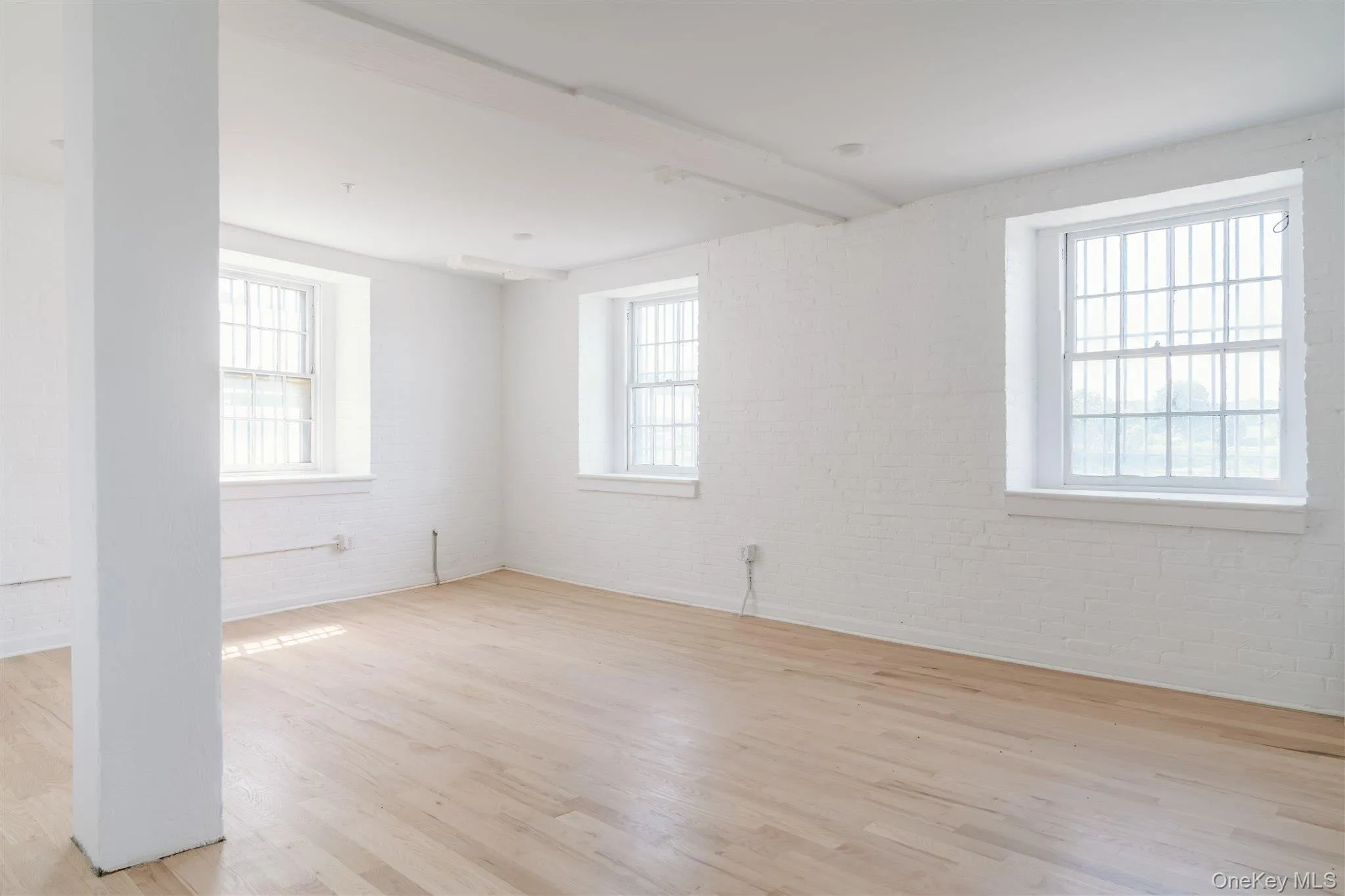Spare room with light wood-style flooring, brick wall, and healthy amount of natural light Spare room with light wood-style flooring, brick wall, and healthy amount of natural light