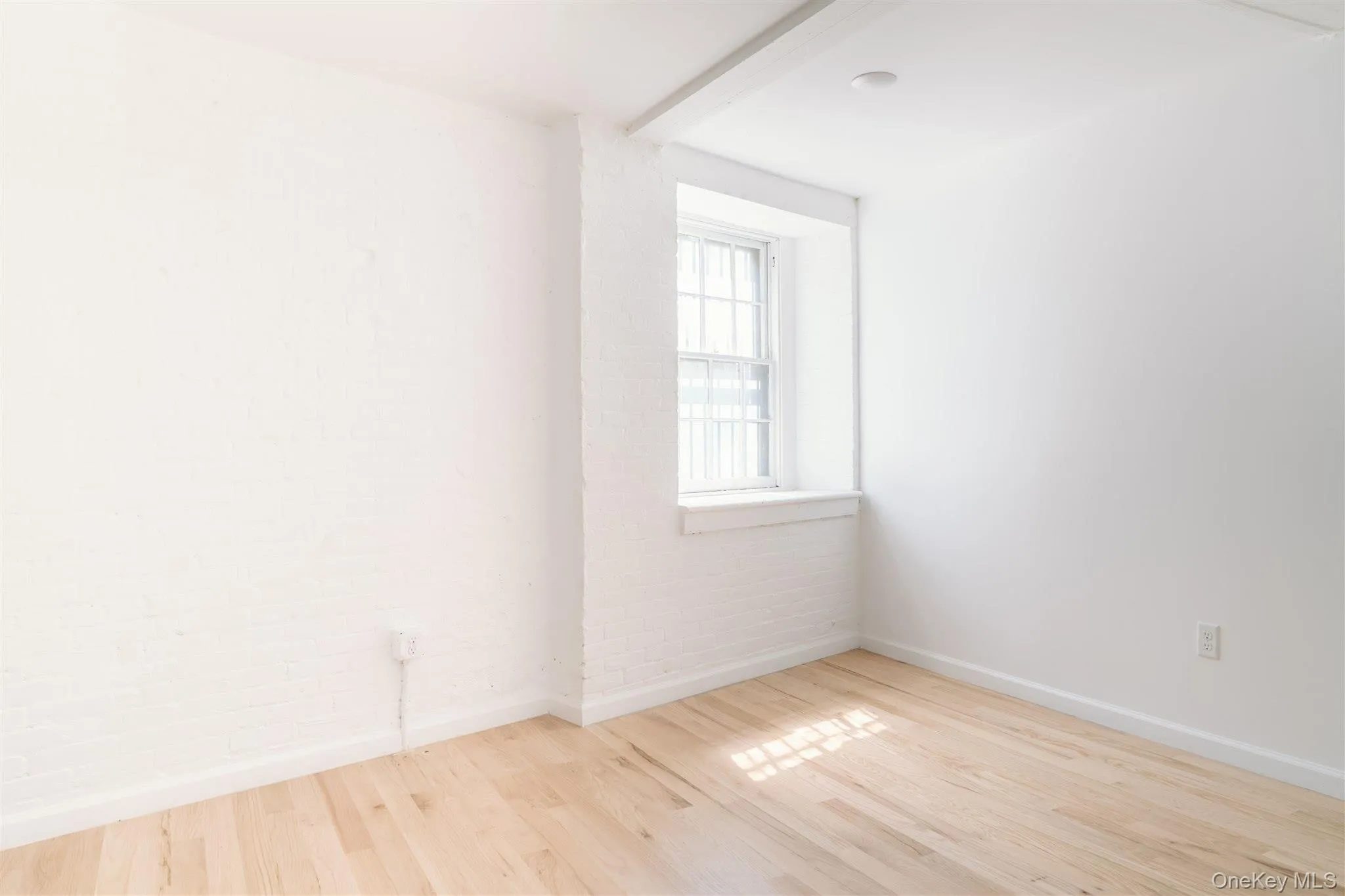 Unfurnished room featuring light wood-type flooring and brick wall Unfurnished room featuring light wood-type flooring and brick wall