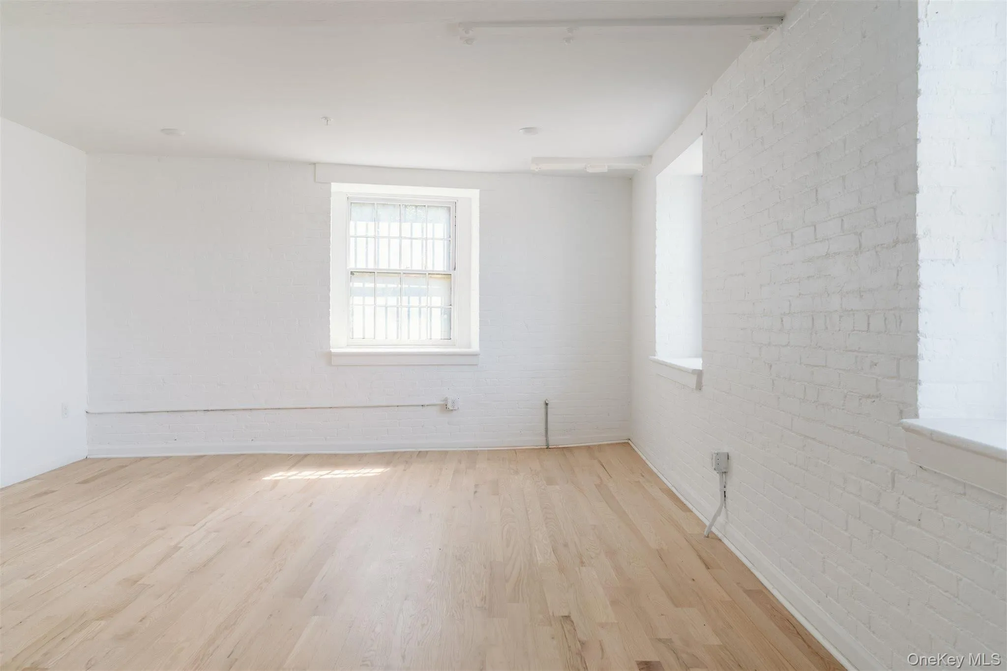 Unfurnished room featuring brick wall and light wood-style flooring Unfurnished room featuring brick wall and light wood-style flooring