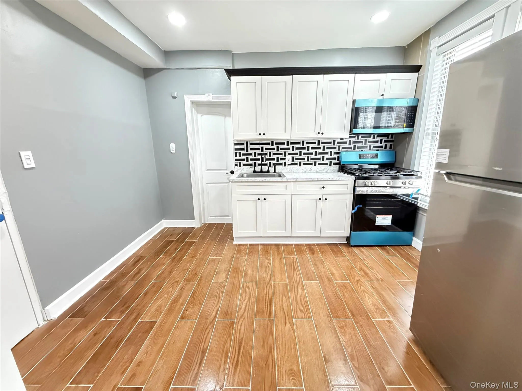 Kitchen featuring appliances with stainless steel finishes, white cabinets, wood finish floors, and decorative backsplash Kitchen featuring appliances with stainless steel finishes, white cabinets, wood finish floors, and decorative backsplash