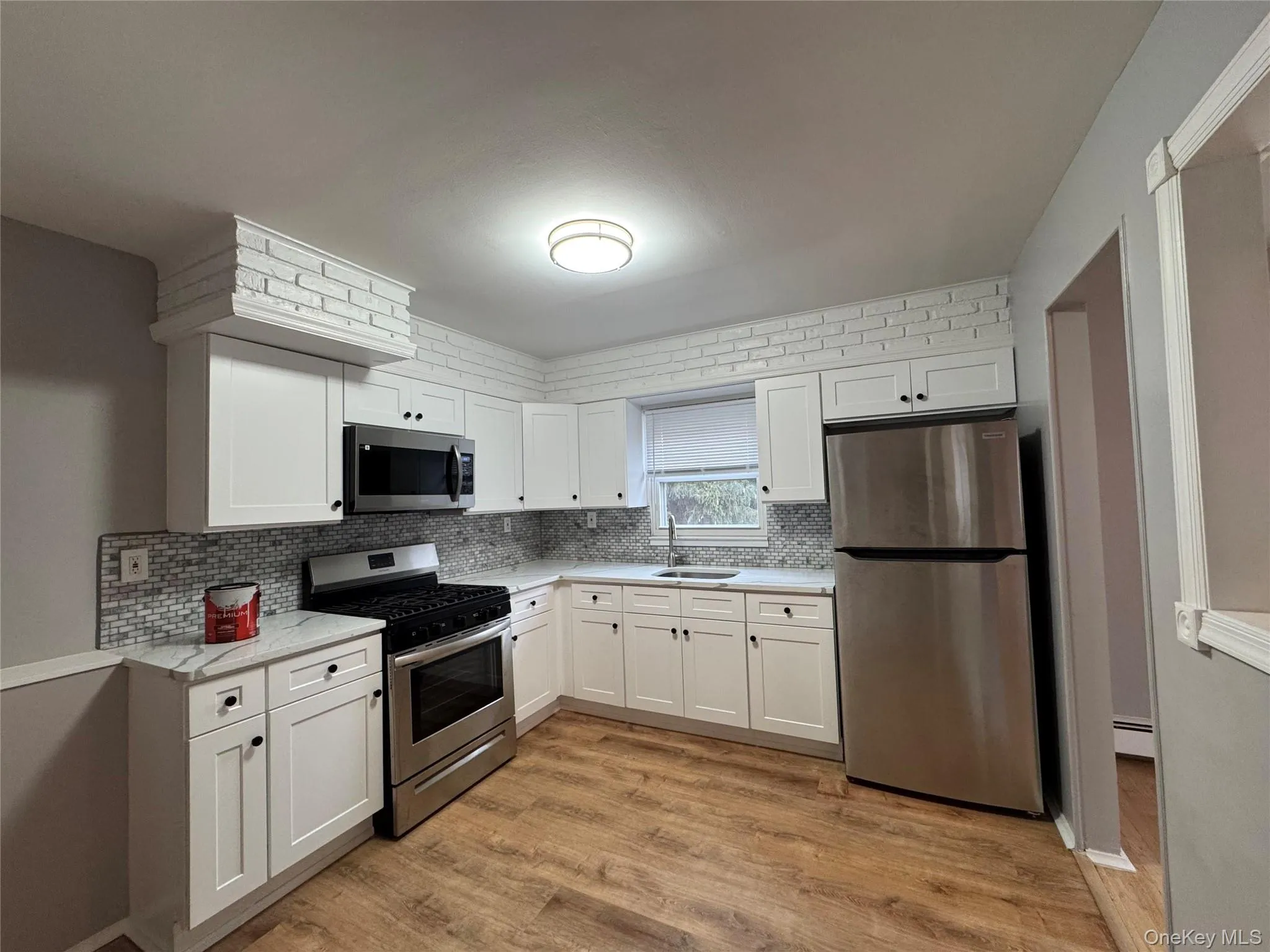 Kitchen with stainless steel appliances, white cabinets, light wood-style floors, light stone countertops, and baseboard heating Kitchen with stainless steel appliances, white cabinets, light wood-style floors, light stone countertops, and baseboard heating