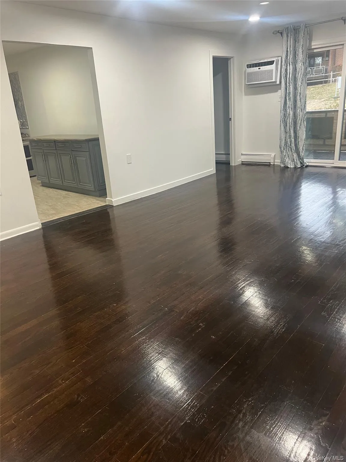 Living room with dark wood-type flooring, a wall unit AC, and a baseboard radiator, balcony access Living room with dark wood-type flooring, a wall unit AC, and a baseboard radiator, balcony access