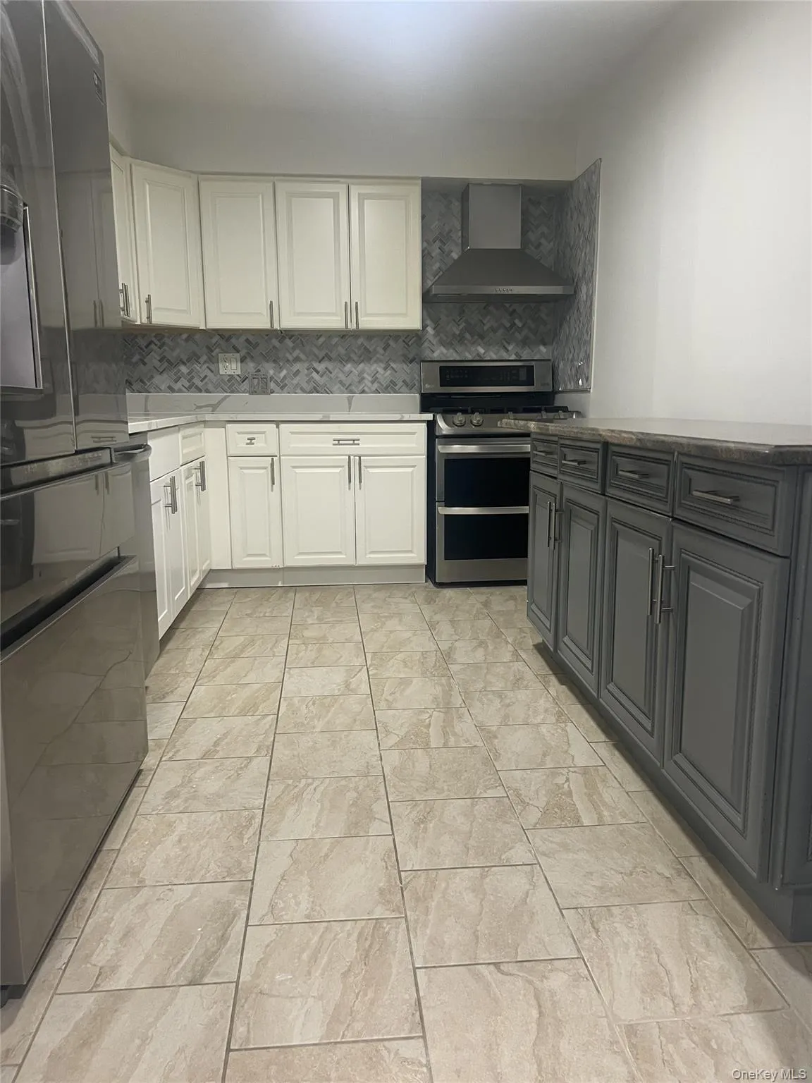 Kitchen with wall chimney range hood, range with two ovens, decorative backsplash, and dark stone counters Kitchen with wall chimney range hood, range with two ovens, decorative backsplash, and dark stone counters