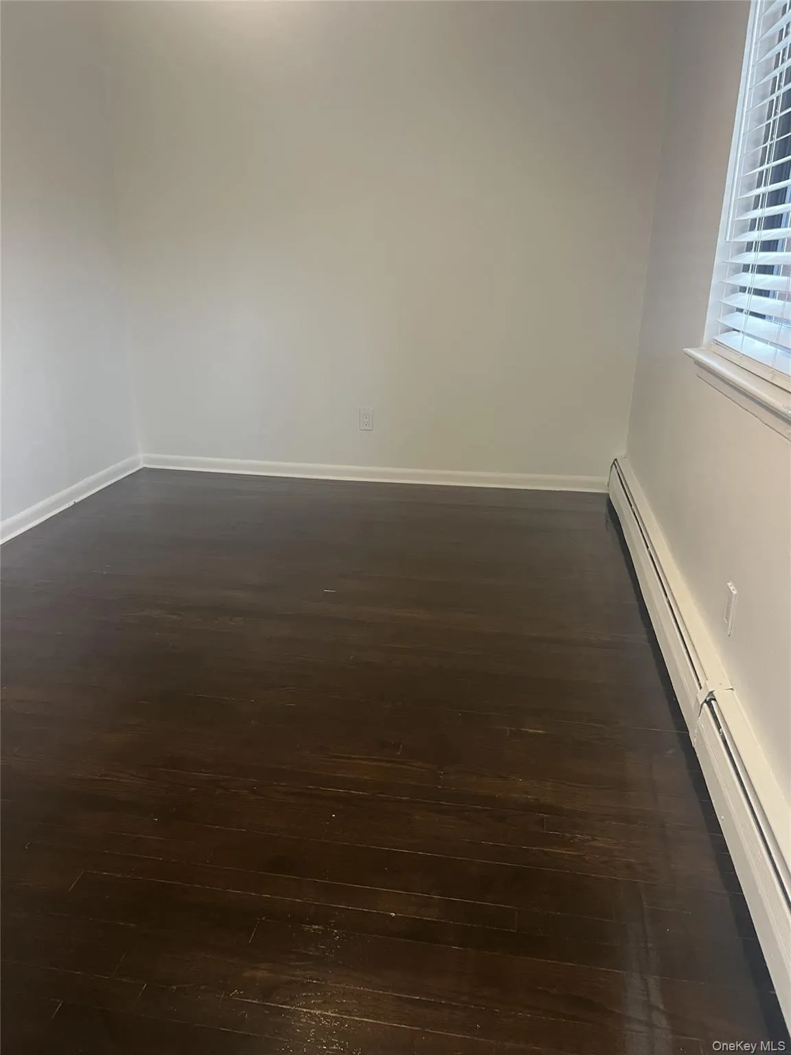 Den room featuring a baseboard heating unit and dark wood-style floors Den room featuring a baseboard heating unit and dark wood-style floors