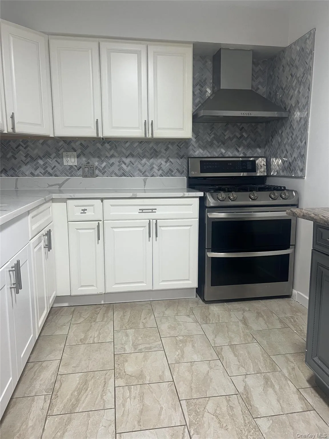 Kitchen with wall chimney exhaust hood, range with two ovens, decorative backsplash, and white cabinetry Kitchen with wall chimney exhaust hood, range with two ovens, decorative backsplash, and white cabinetry