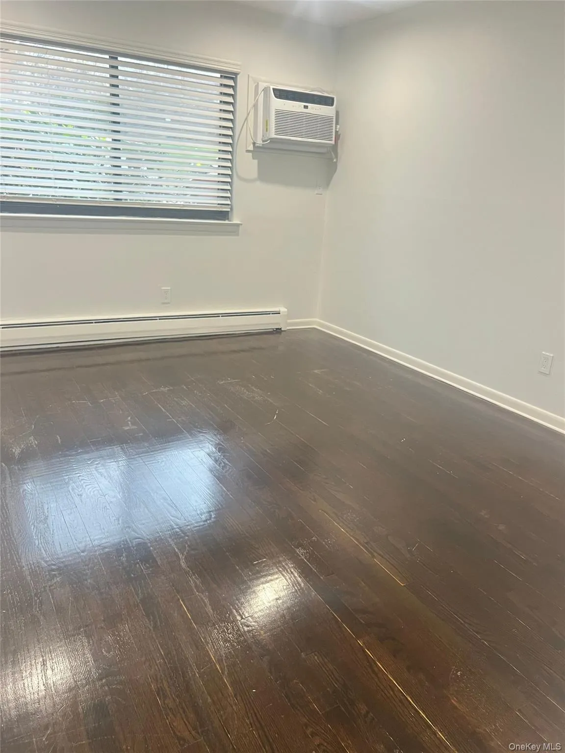 Spare room with baseboard heating, dark wood-style flooring, and a wall unit AC Spare room with baseboard heating, dark wood-style flooring, and a wall unit AC