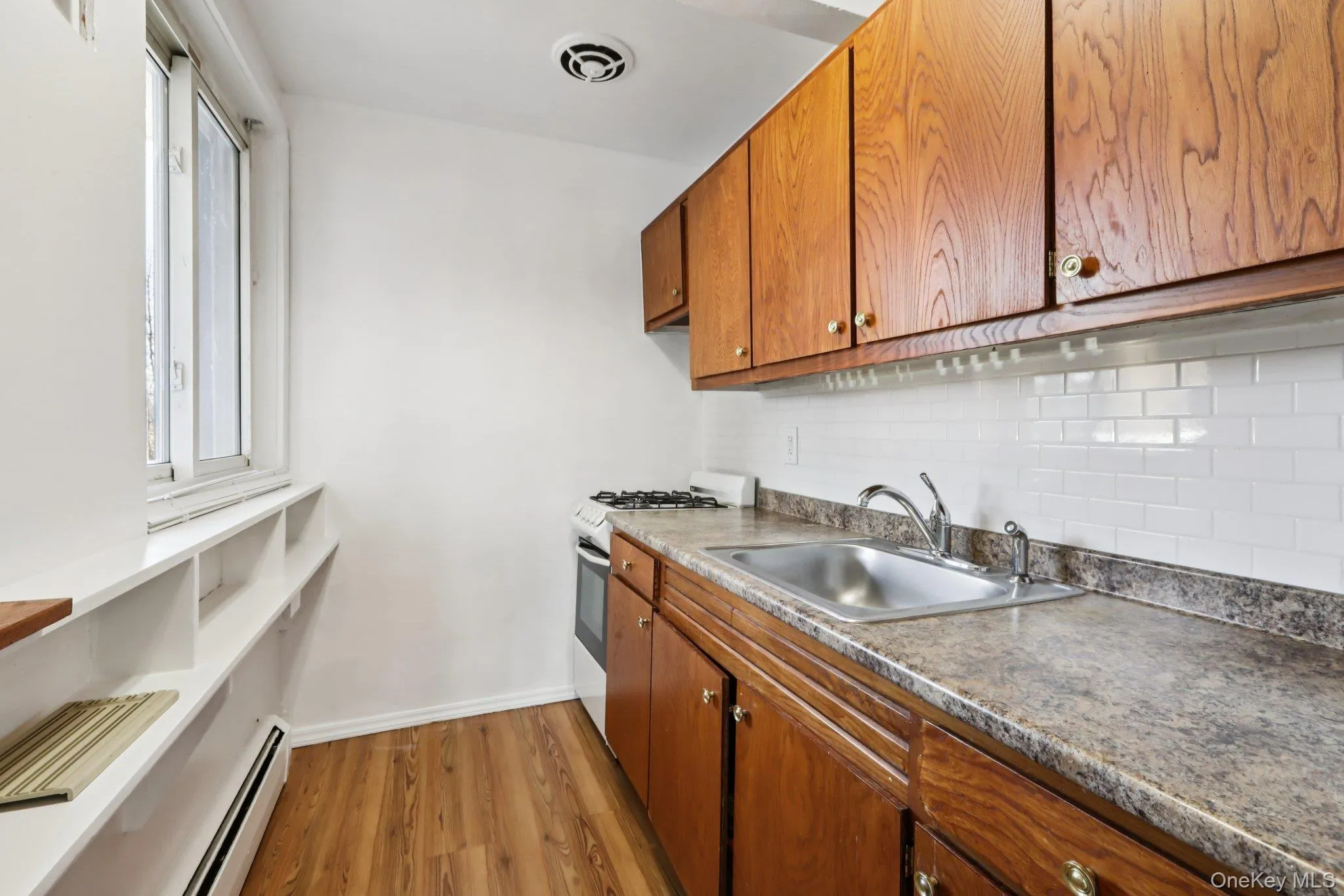 Kitchen featuring brown cabinetry, range with gas cooktop, a baseboard heating unit, tasteful backsplash, and light wood-style floors Kitchen featuring brown cabinetry, range with gas cooktop, a baseboard heating unit, tasteful backsplash, and light wood-style floors