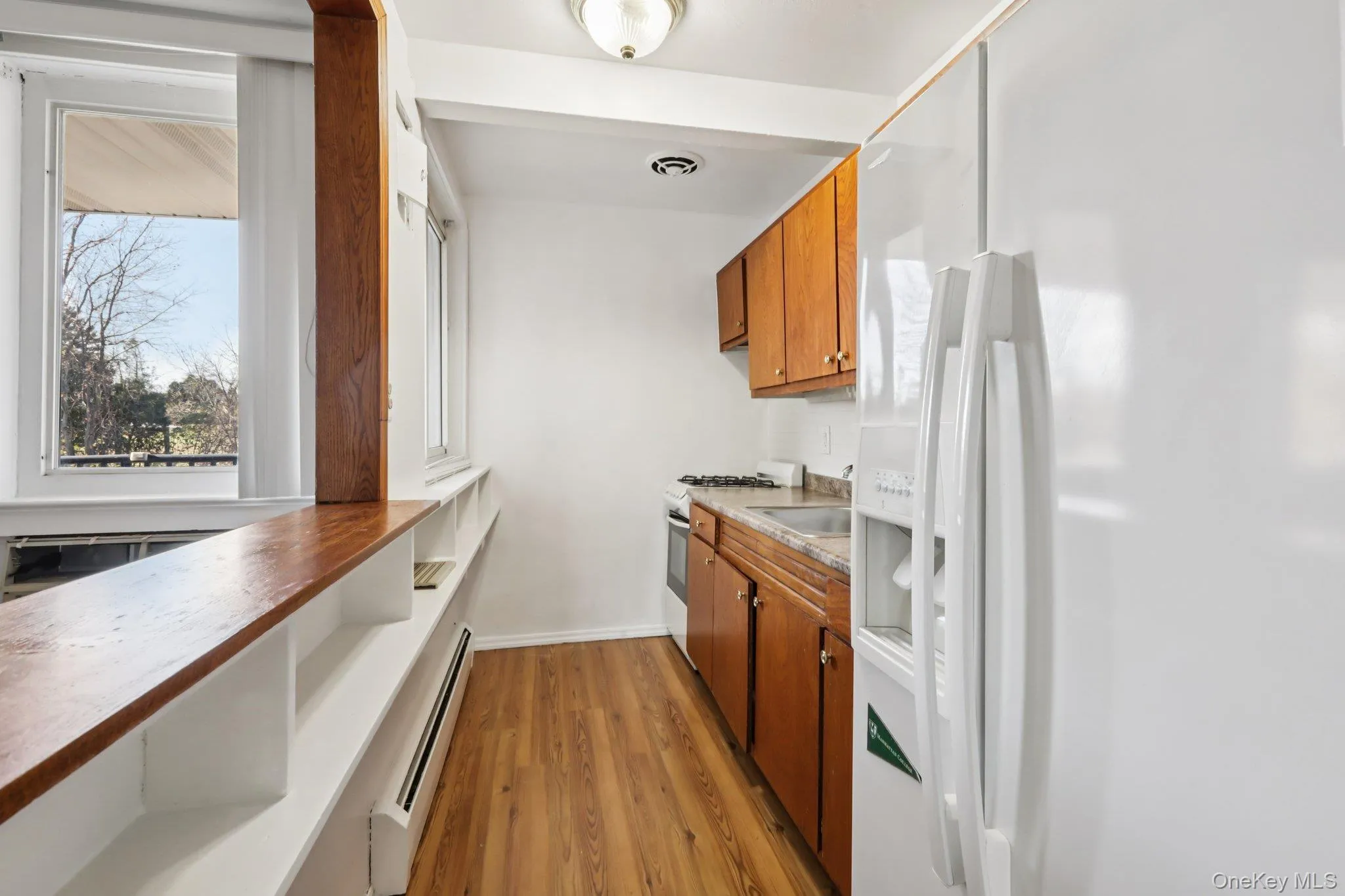 Kitchen with white refrigerator with ice dispenser, wooden counters, a baseboard heating unit, light wood-type flooring, and brown cabinetry Kitchen with white refrigerator with ice dispenser, wooden counters, a baseboard heating unit, light wood-type flooring, and brown cabinetry